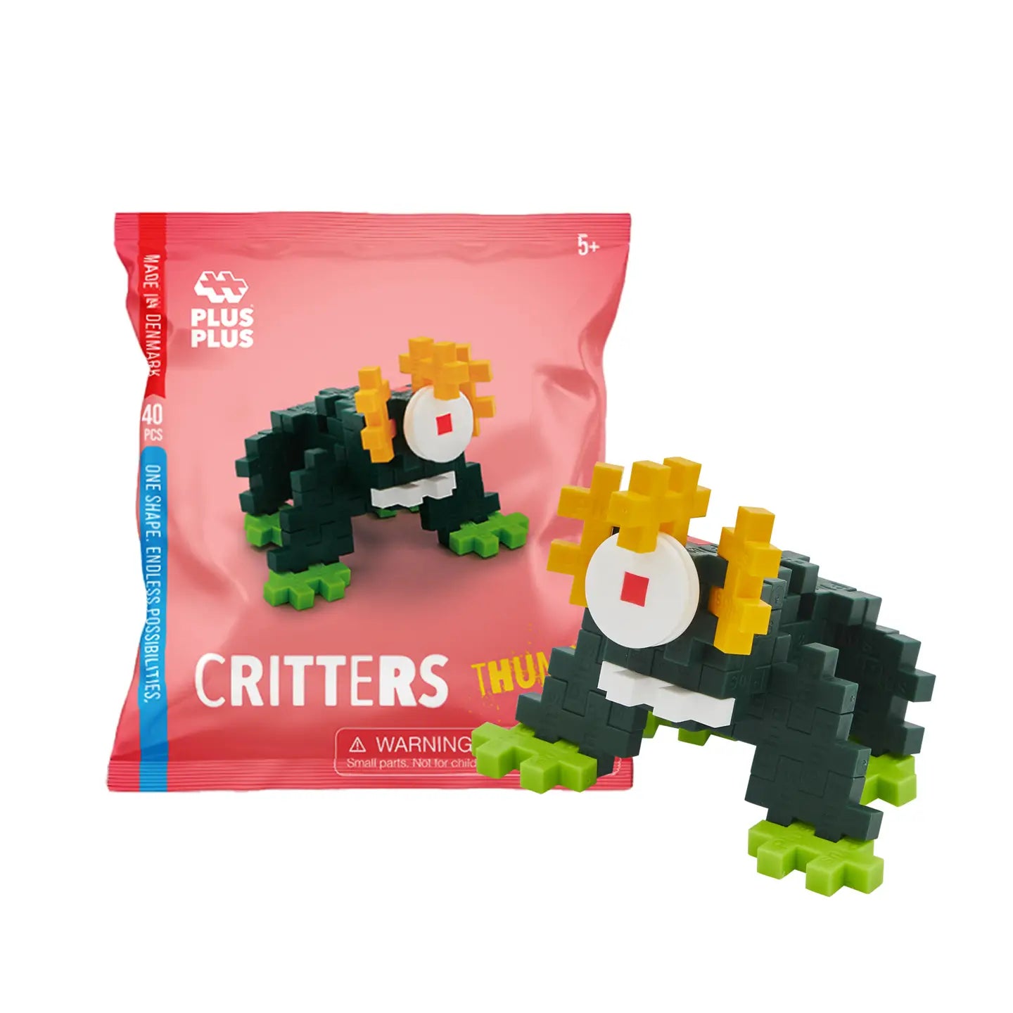 Toy figure of a black and green creature with a red circle on a pink Plus Plus packaging.