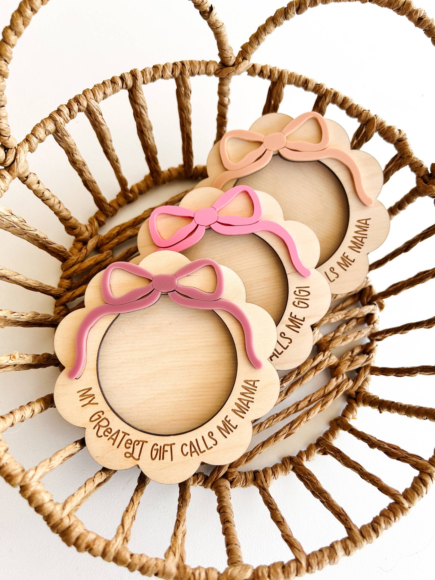 Wooden baby booties with pink bows and engraved text on a woven basket background