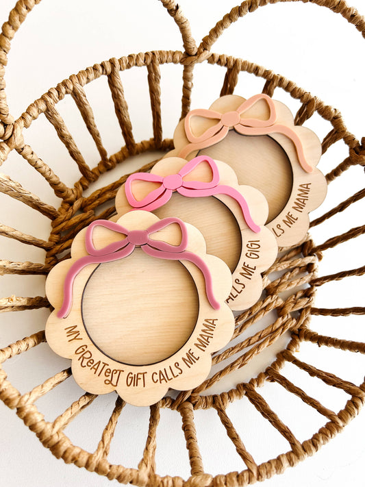 Wooden baby booties with pink bows and engraved text on a woven basket background