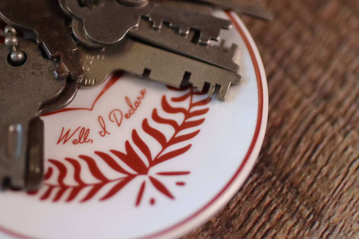 Close-up of a keychain with keys and a decorative plate featuring red leaf design and text.