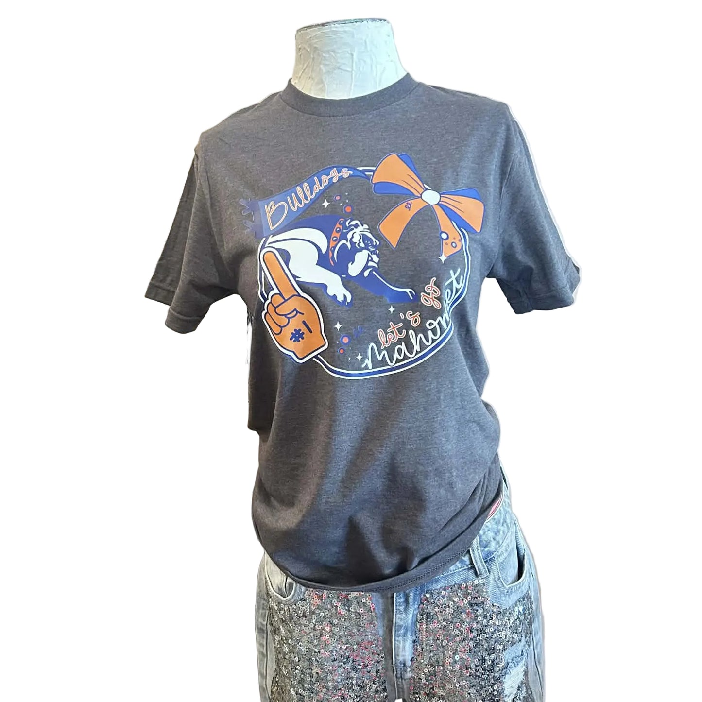 Grey T-Shirt with a graphic showing an orange foam finger that says #1, a blue pennant that reads "bulldogs", an orange and blue bow, the Bulldog mascot and text that says "Let's Go Mahomet" on a mannequin with a  white background