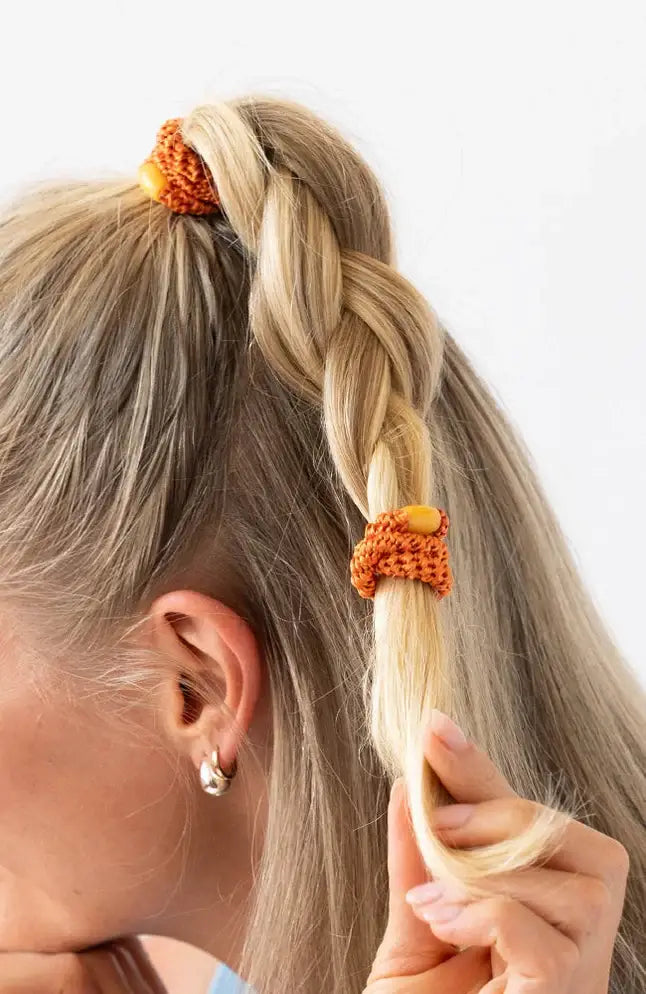 Person with braided hair using orange hair ties on a white background
