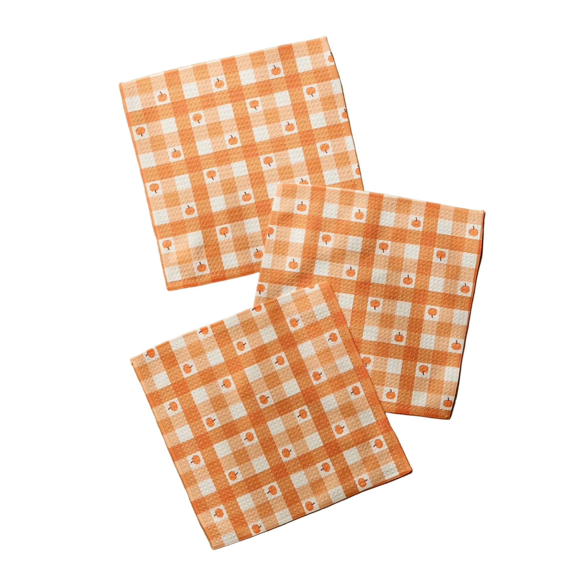 Three square cotton napkins with an orange and white gingham check pattern and small floral motifs, arranged on a light wood surface.