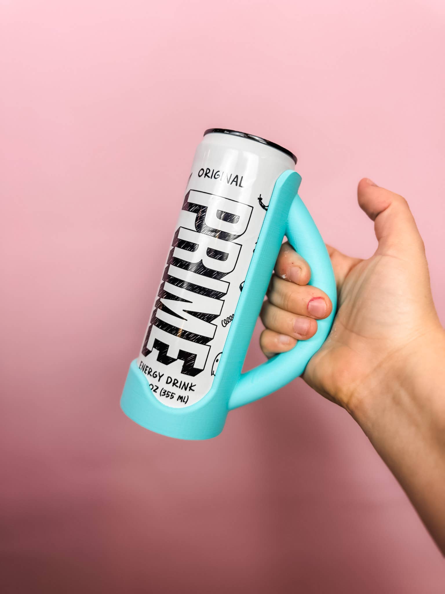 Hand holding a can of Prime energy drink with a pink background