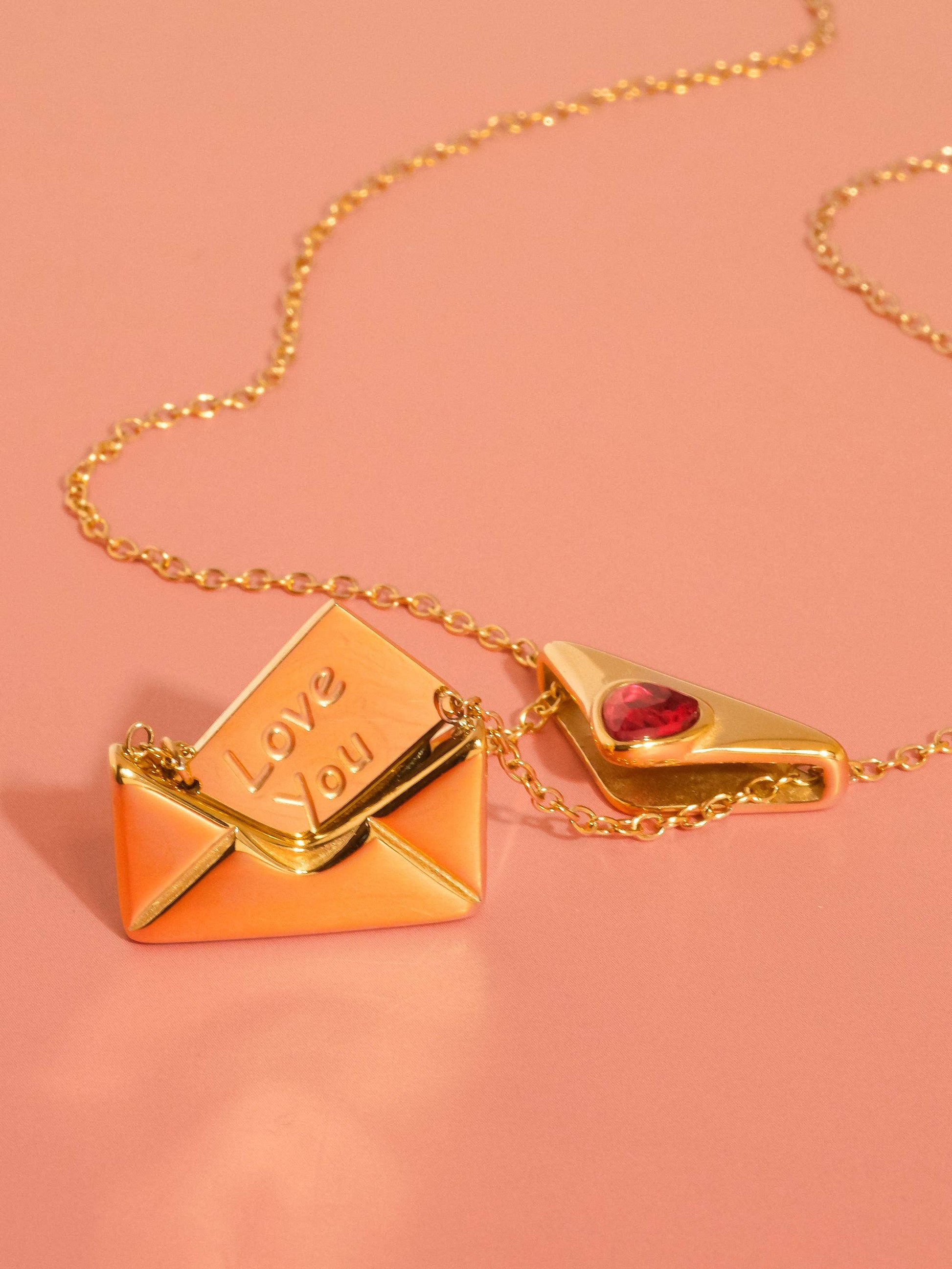 Gold necklace with heart and envelope pendants on a pink background