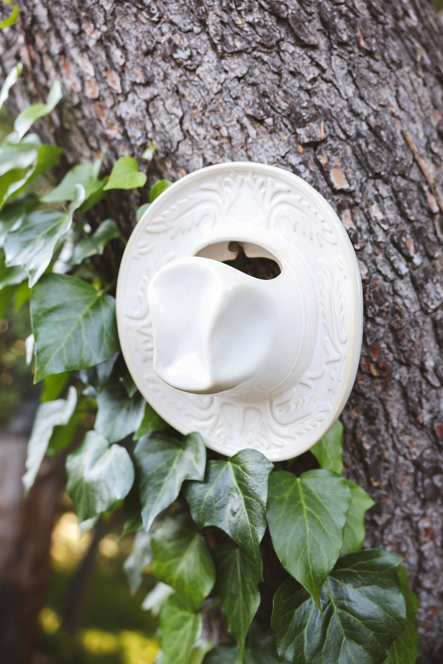 White ceramic cowboy hat shaped vase hanging on a tree 