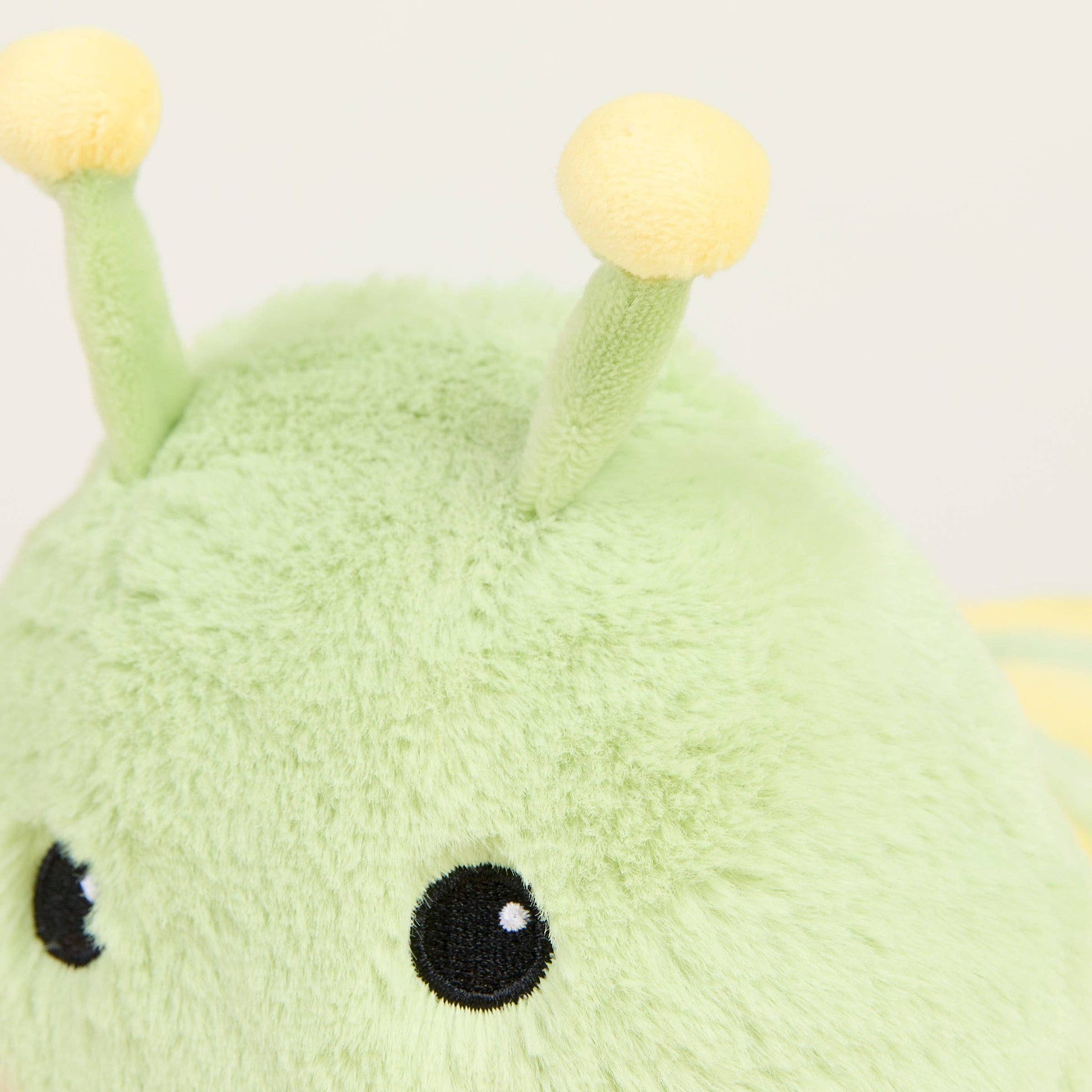 Close-up of a green plush caterpillar with yellow antennae on a light background