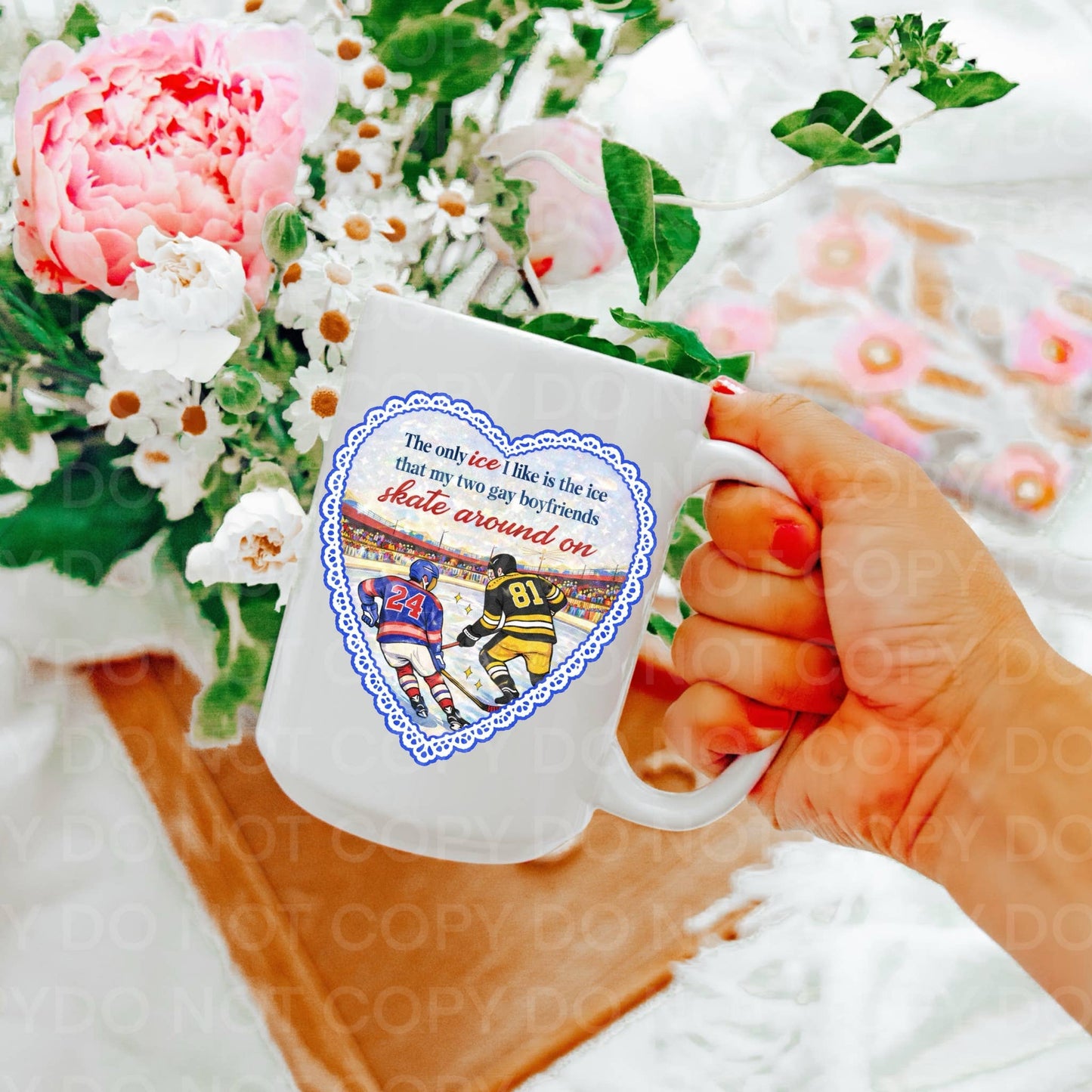 Hand holding a mug with a hockey design and text, surrounded by flowers.