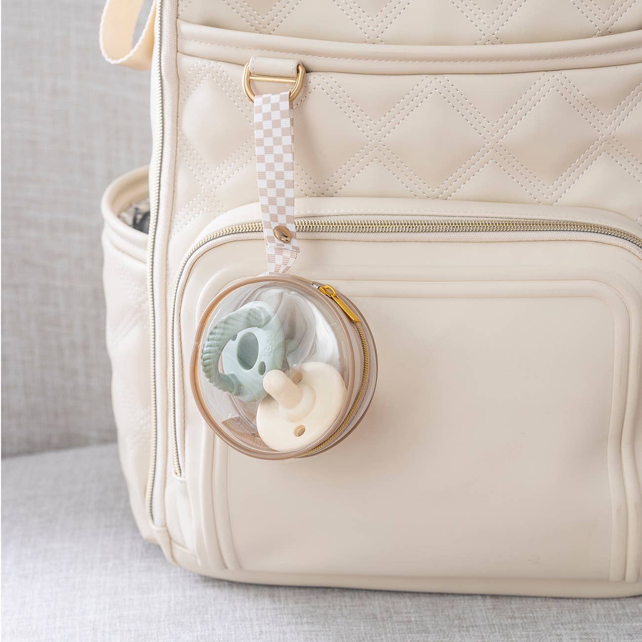 Round clear pacifier holder clipped onto a diaper bag