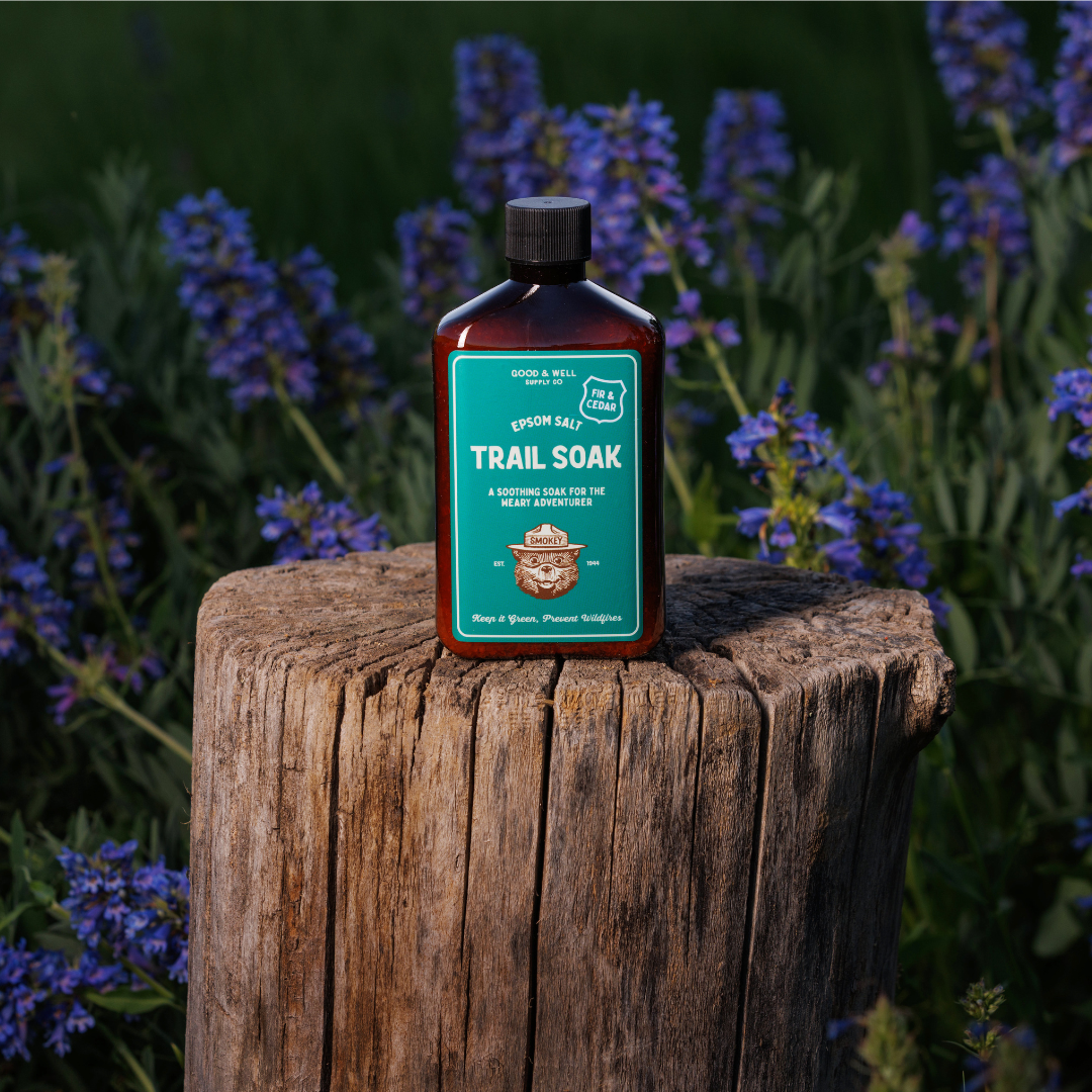 Trail Soak bottle on a wooden stump with purple flowers in the background