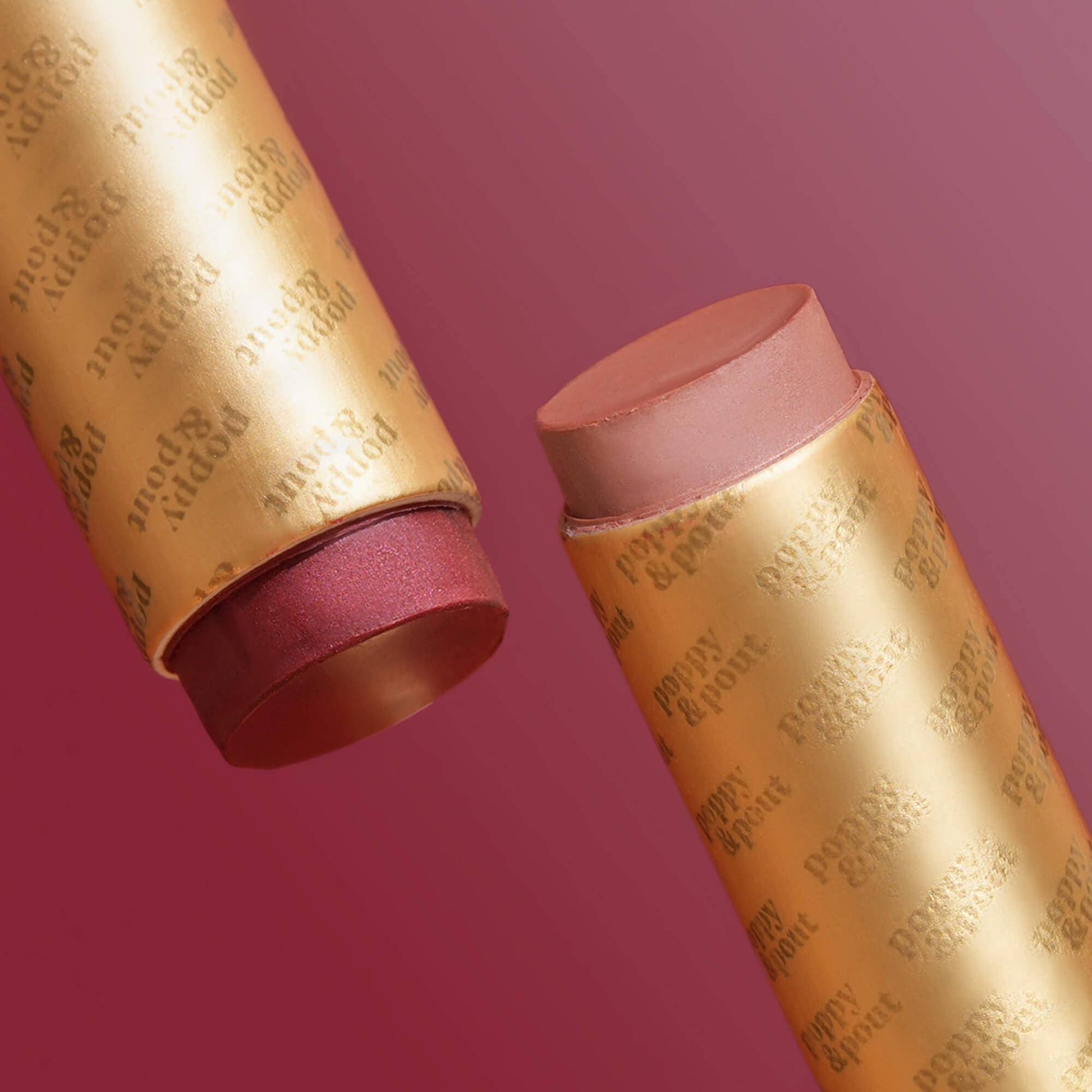 Two makeup sticks with gold packaging on a pink background