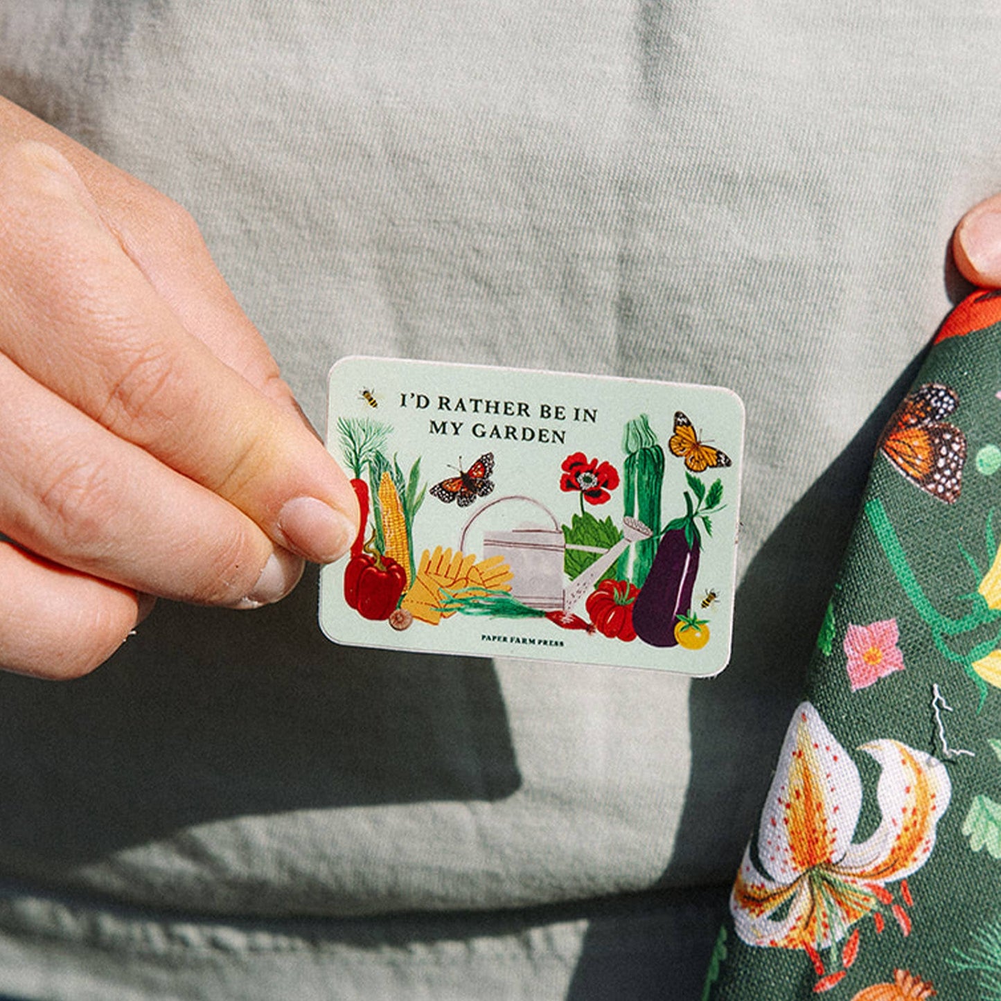 Person holding a small card with garden-themed illustrations and text.