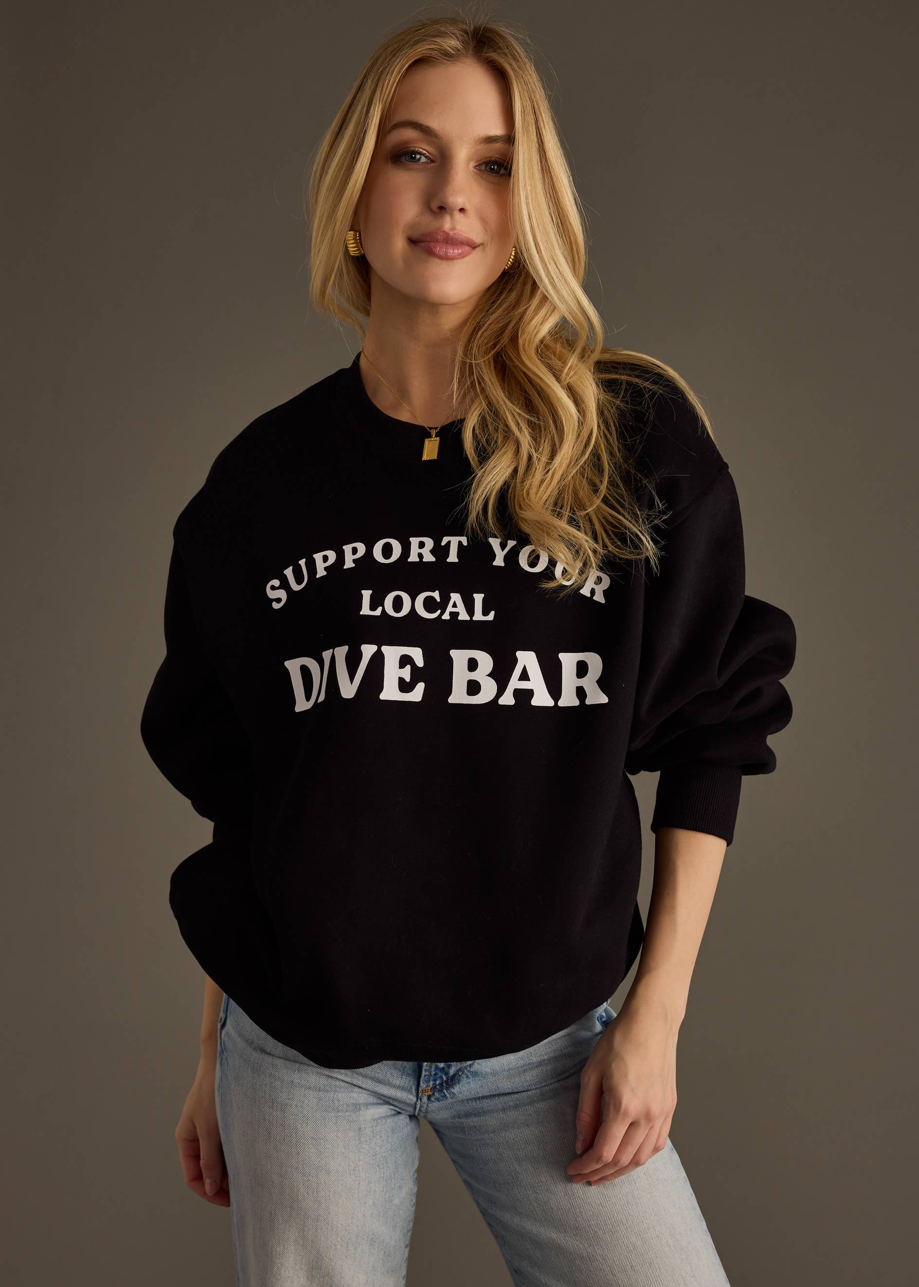 Woman wearing a black sweatshirt with 'Support Your Local Dive Bar' text on a plain background
