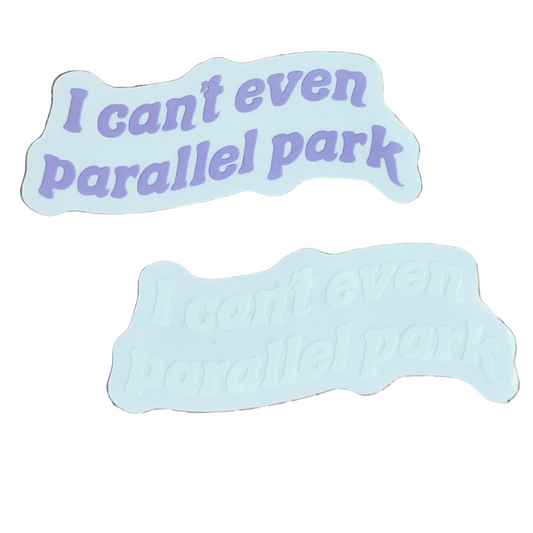 Two die-cut stickers with the phrase 'I can't even parallel park' in purple text, one shown as a flat printed piece and the other as a raised 3D sticker, placed on a woven straw mat with star-shaped confetti.