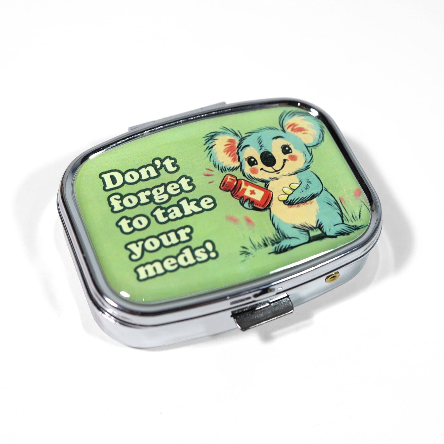 Pill box with a cartoon koala and text 'Don't forget to take your meds!' on a green background