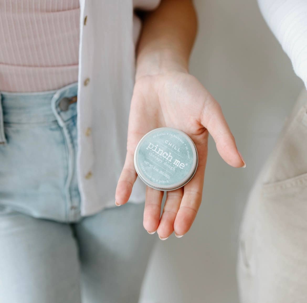 Hand holding a small round container labeled 'pinch me' against a neutral background
