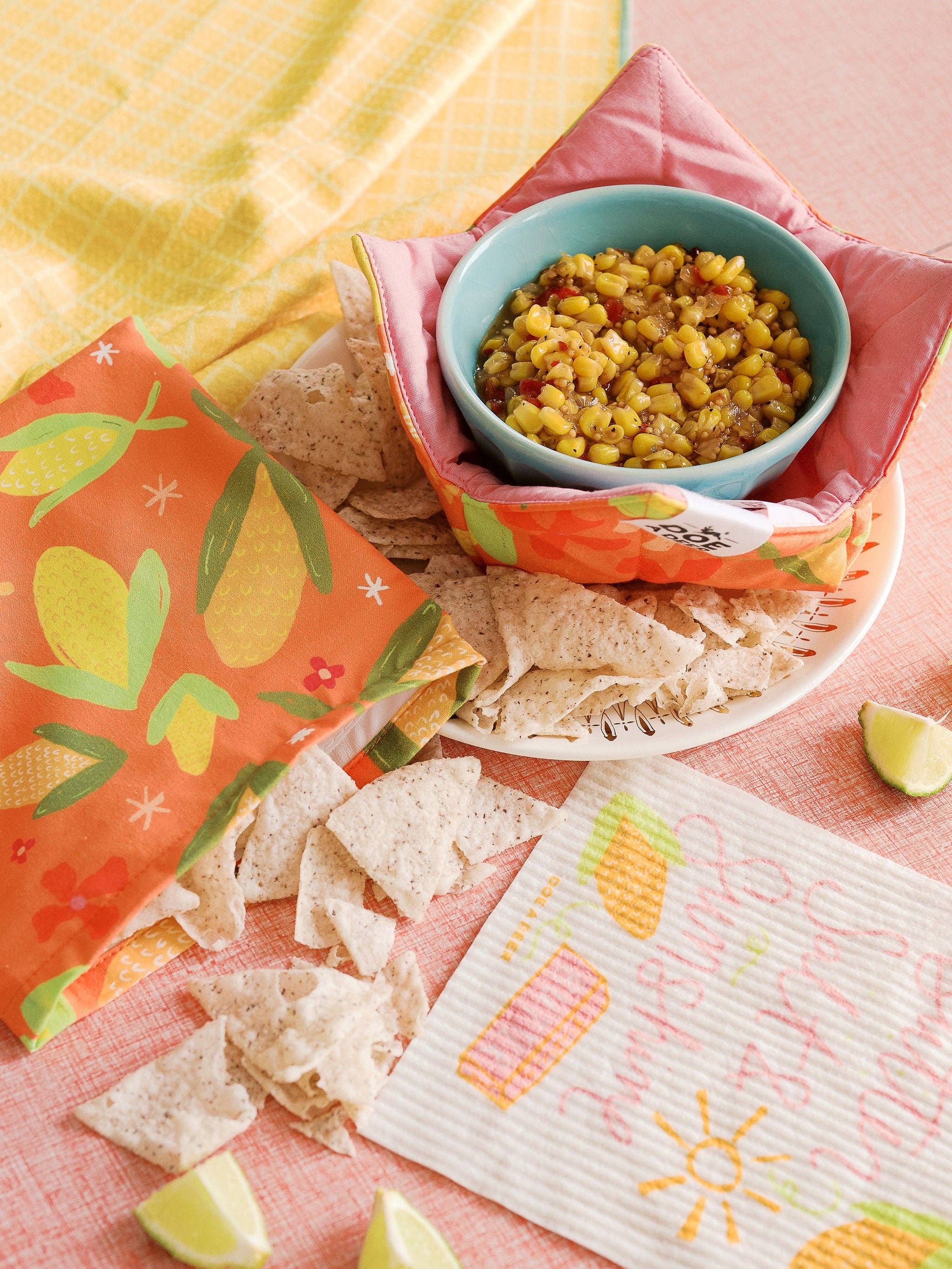 Tortilla chips and a bowl of corn salsa on a colorful tablecloth.