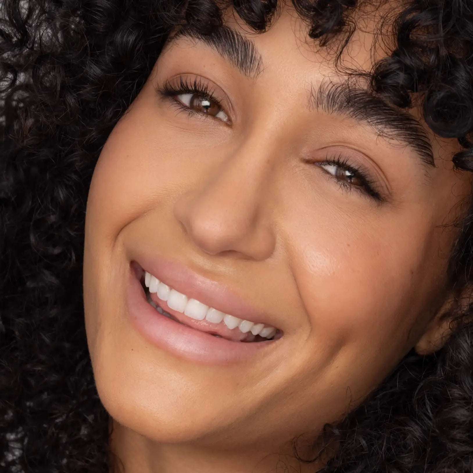 Close-up of a woman with a bright smile and curly hair.