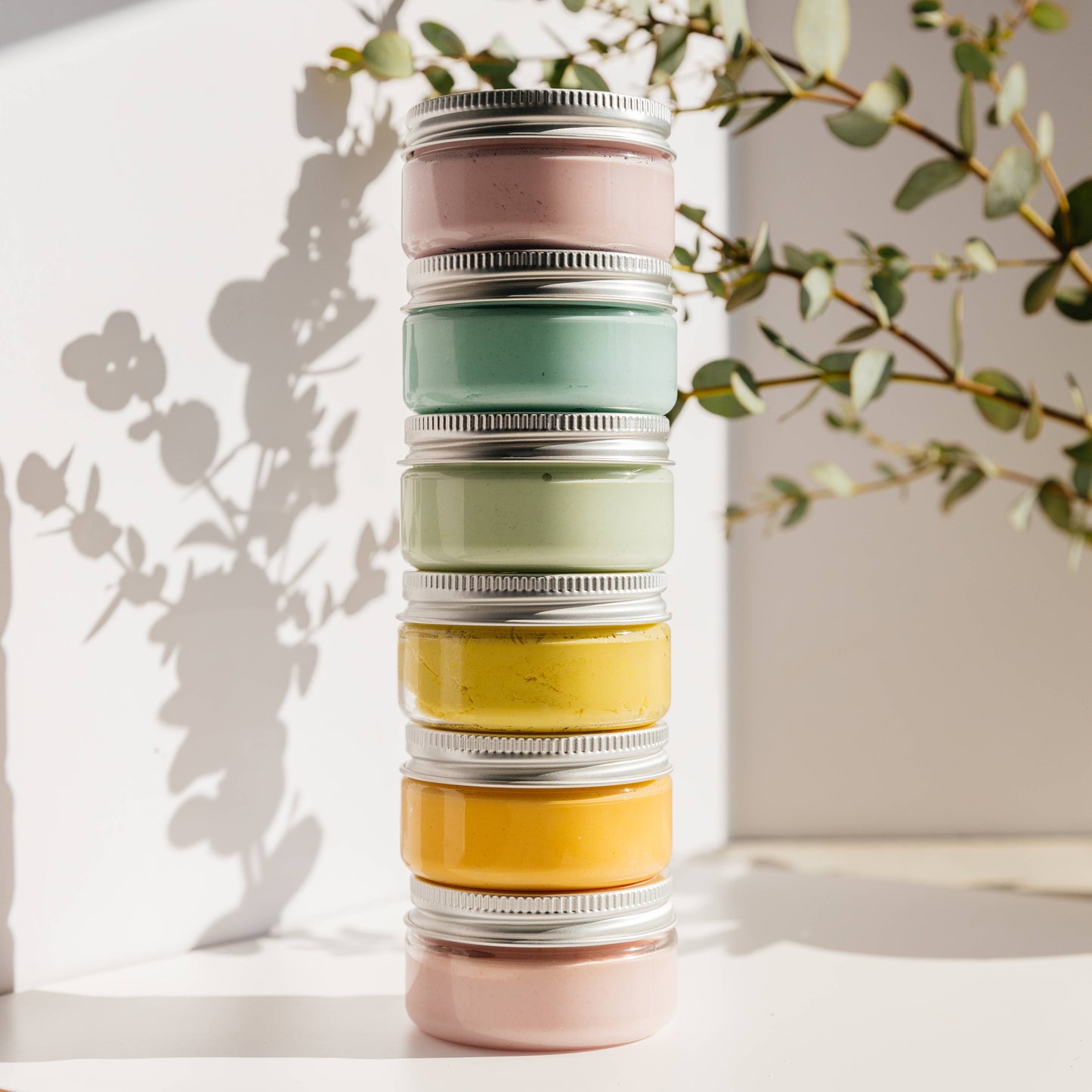 Stack of colorful jars with metal lids on a light surface with a plant in the background