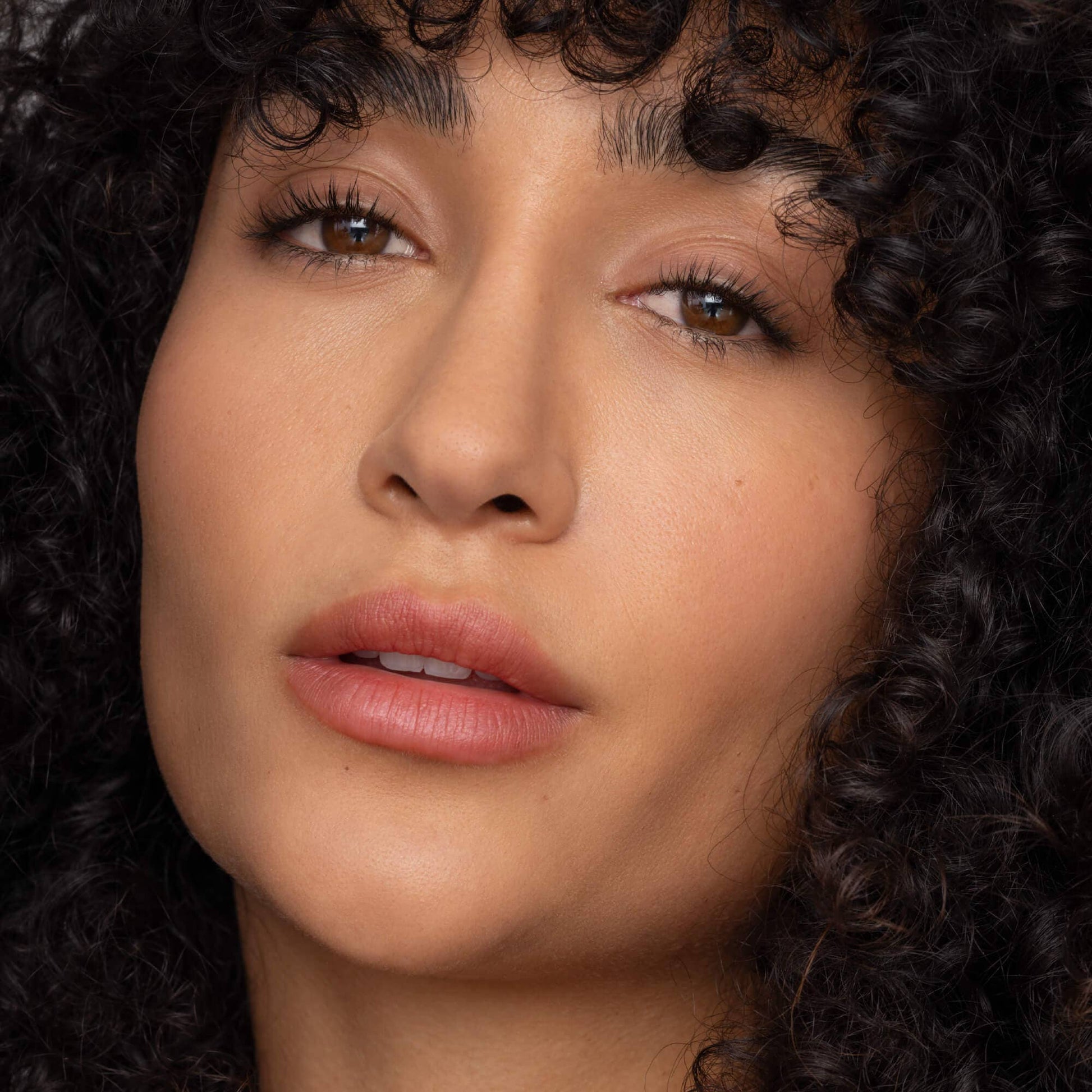 Close-up of a woman with curly hair and pink lipstick.