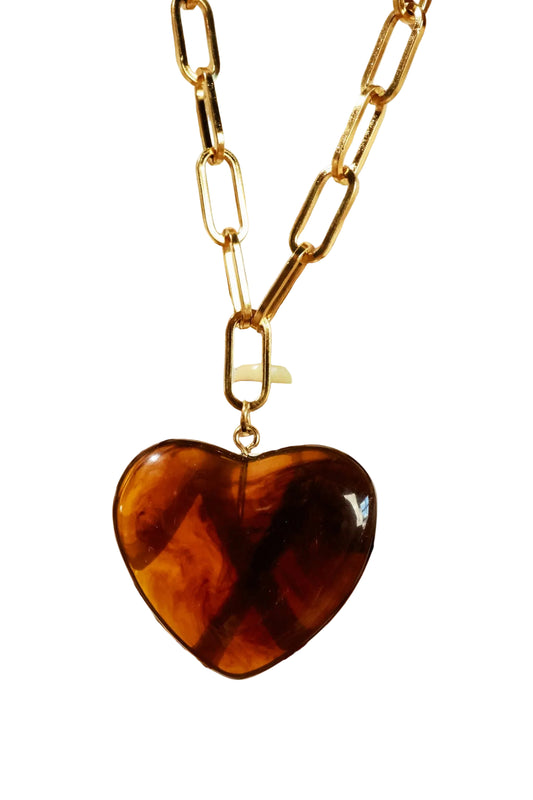 Heart-shaped tortoiseshell pendant on a gold chain against a wooden lattice background