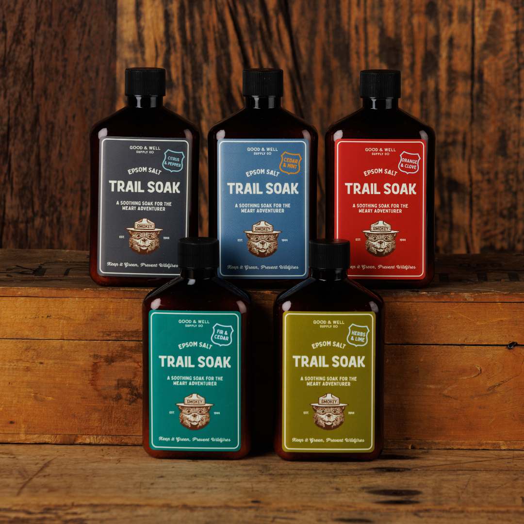 Five bottles of 'Trail Soak' with colorful labels on a wooden surface.