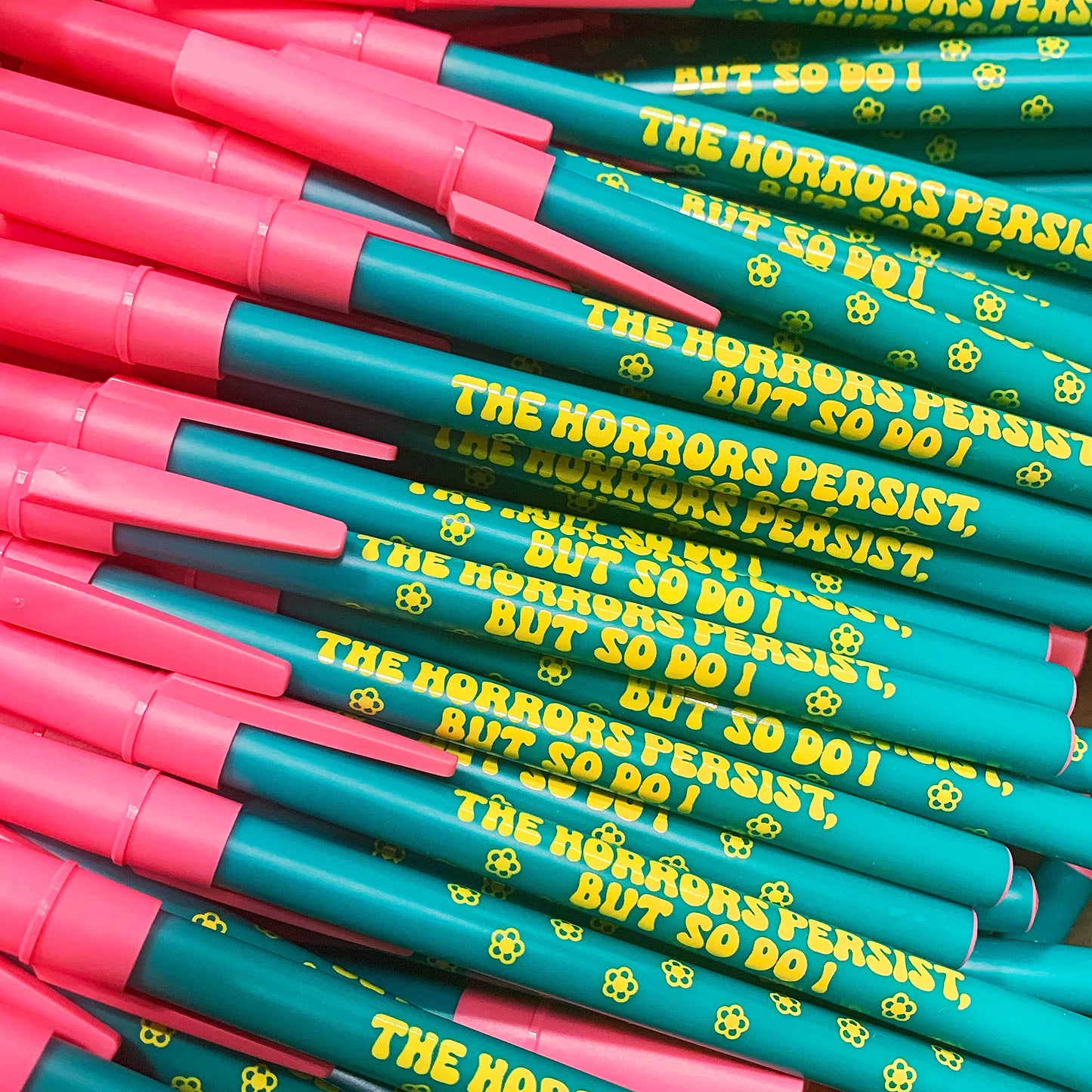 Stack of pens with teal and pink bodies and yellow text.