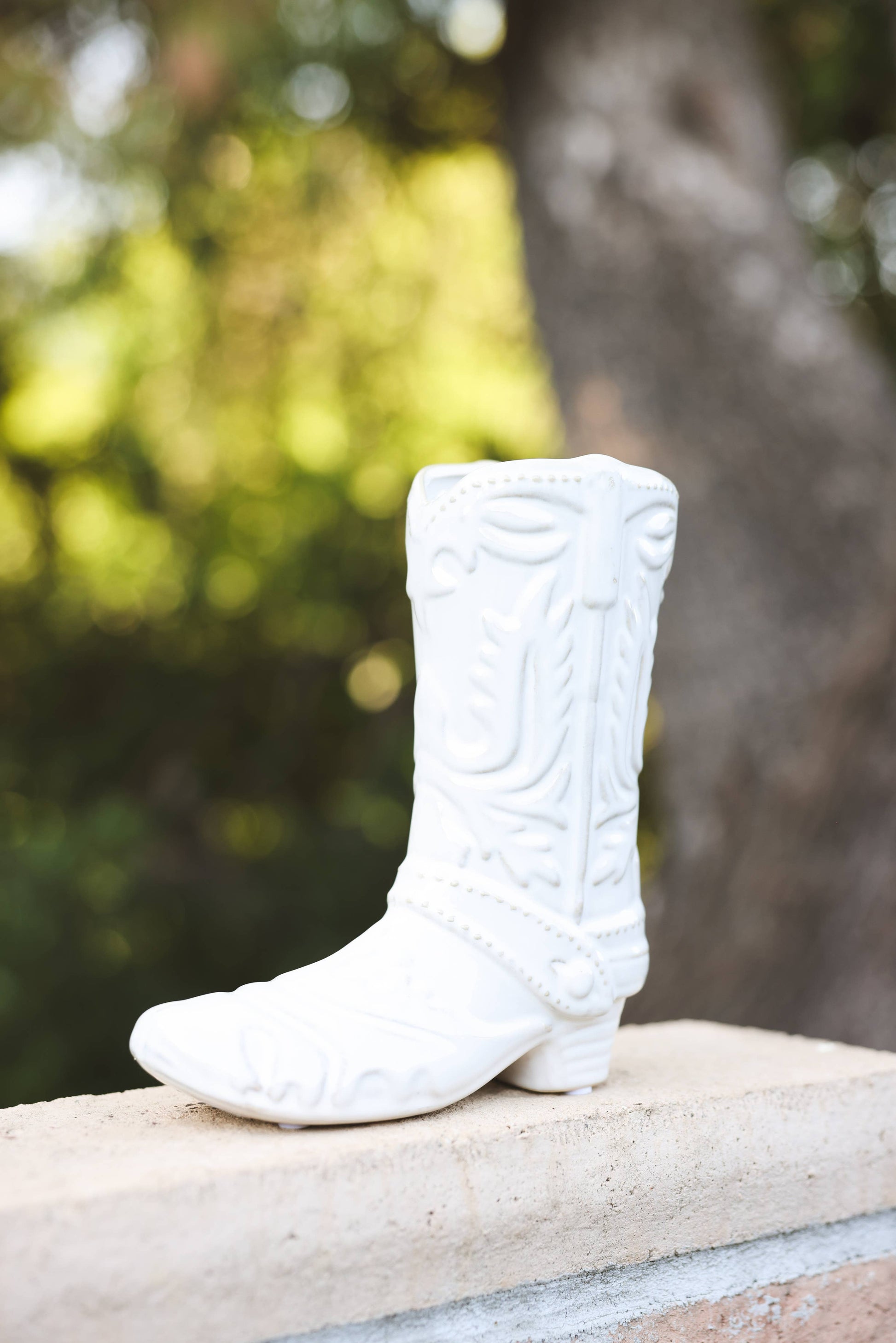 White ceramic cowboy boot on a stone ledge with a blurred natural background