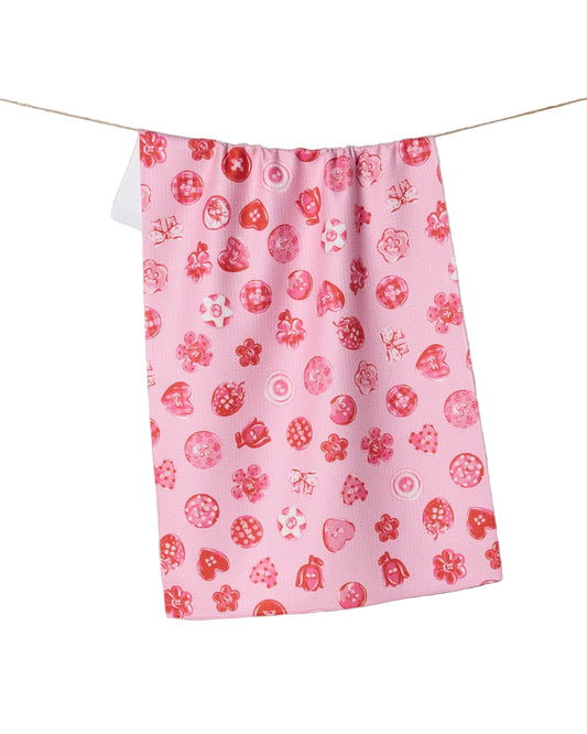 Pink towel with red buttons pattern hanging on a line against a neutral background