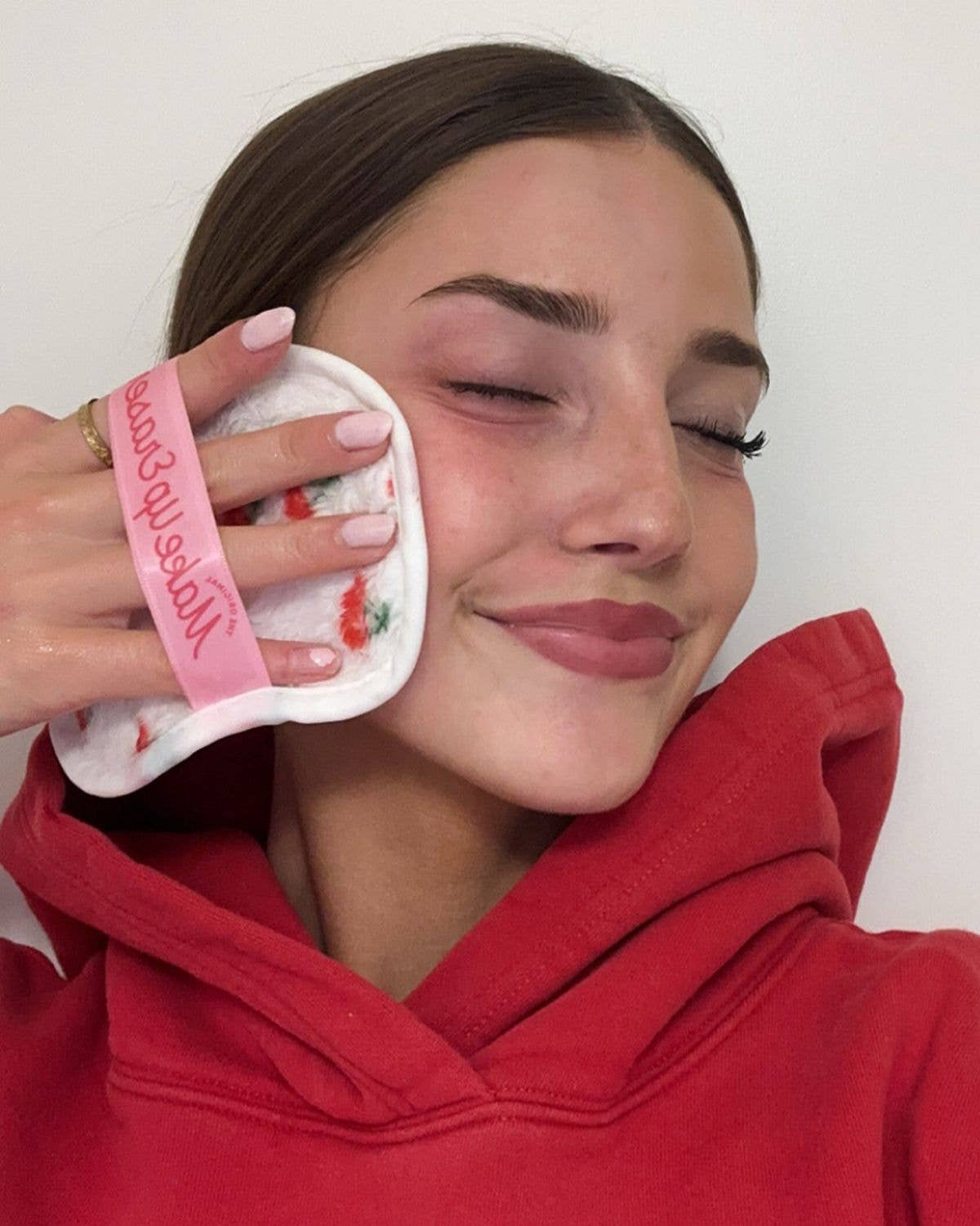 Person wearing a red hoodie with a white cloth on their face against a plain background