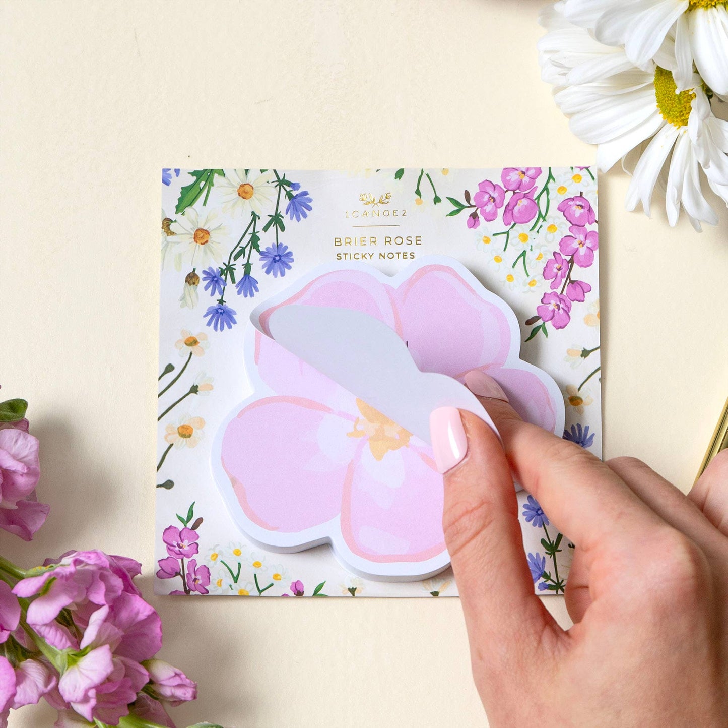 Hand holding pink bunny-shaped sticky notes with floral design in the background