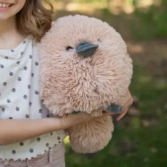 Person holding a fluffy beige toy in a natural setting