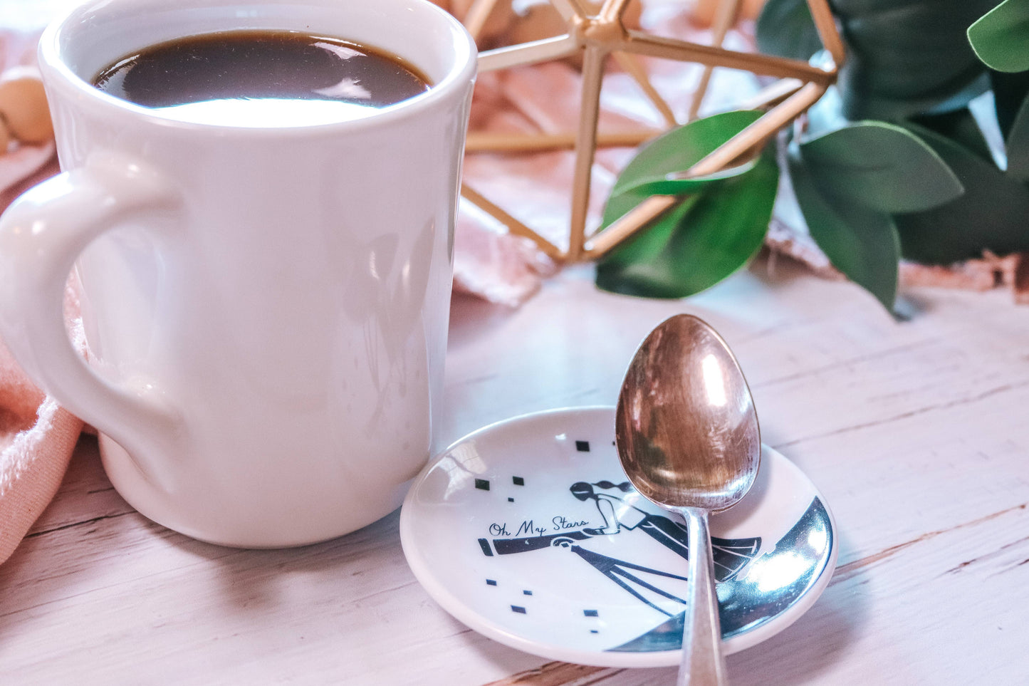 White mug with coffee, spoon, and decorative elements on a wooden surface