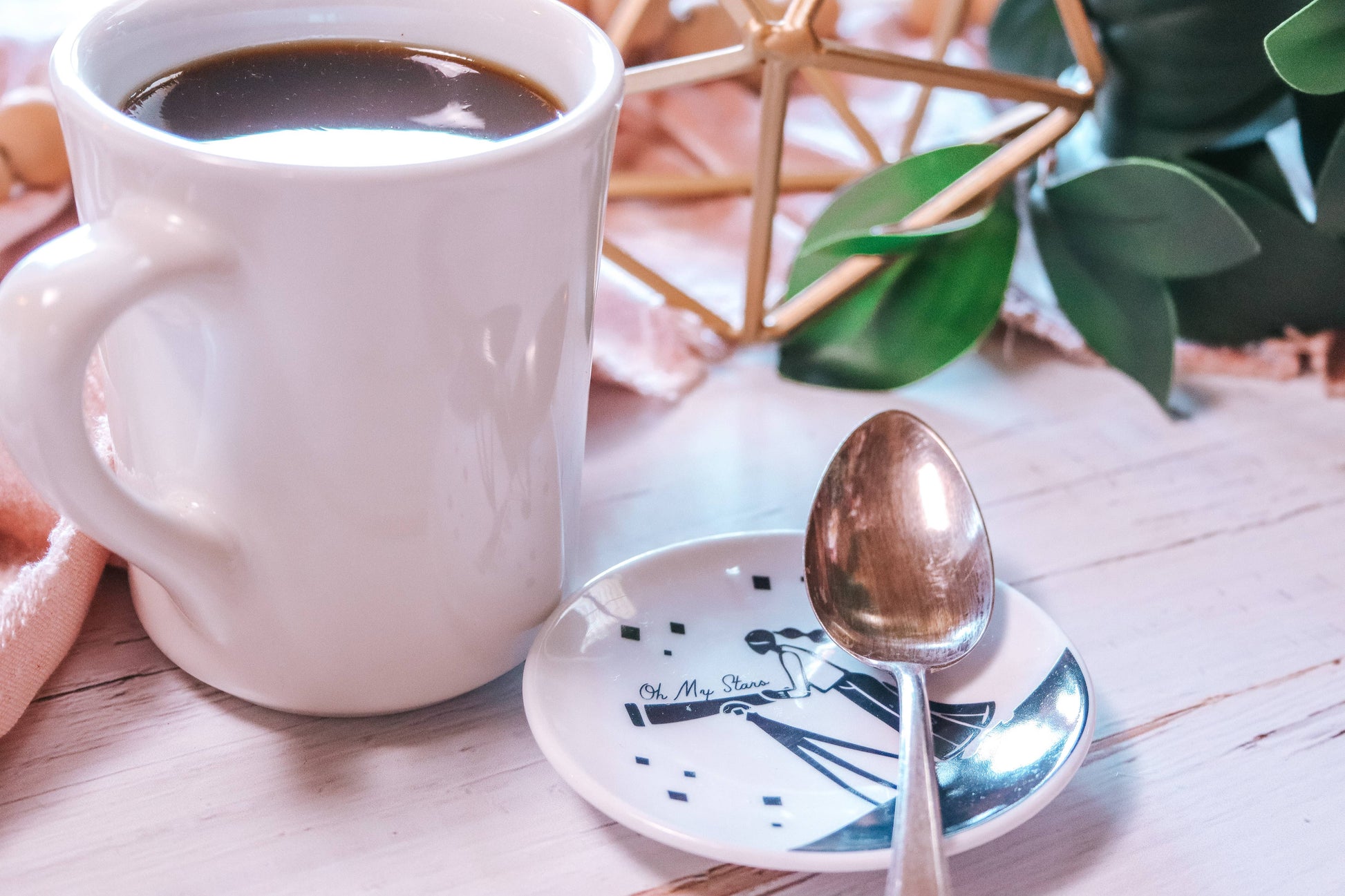 White mug with coffee, spoon, and decorative elements on a wooden surface