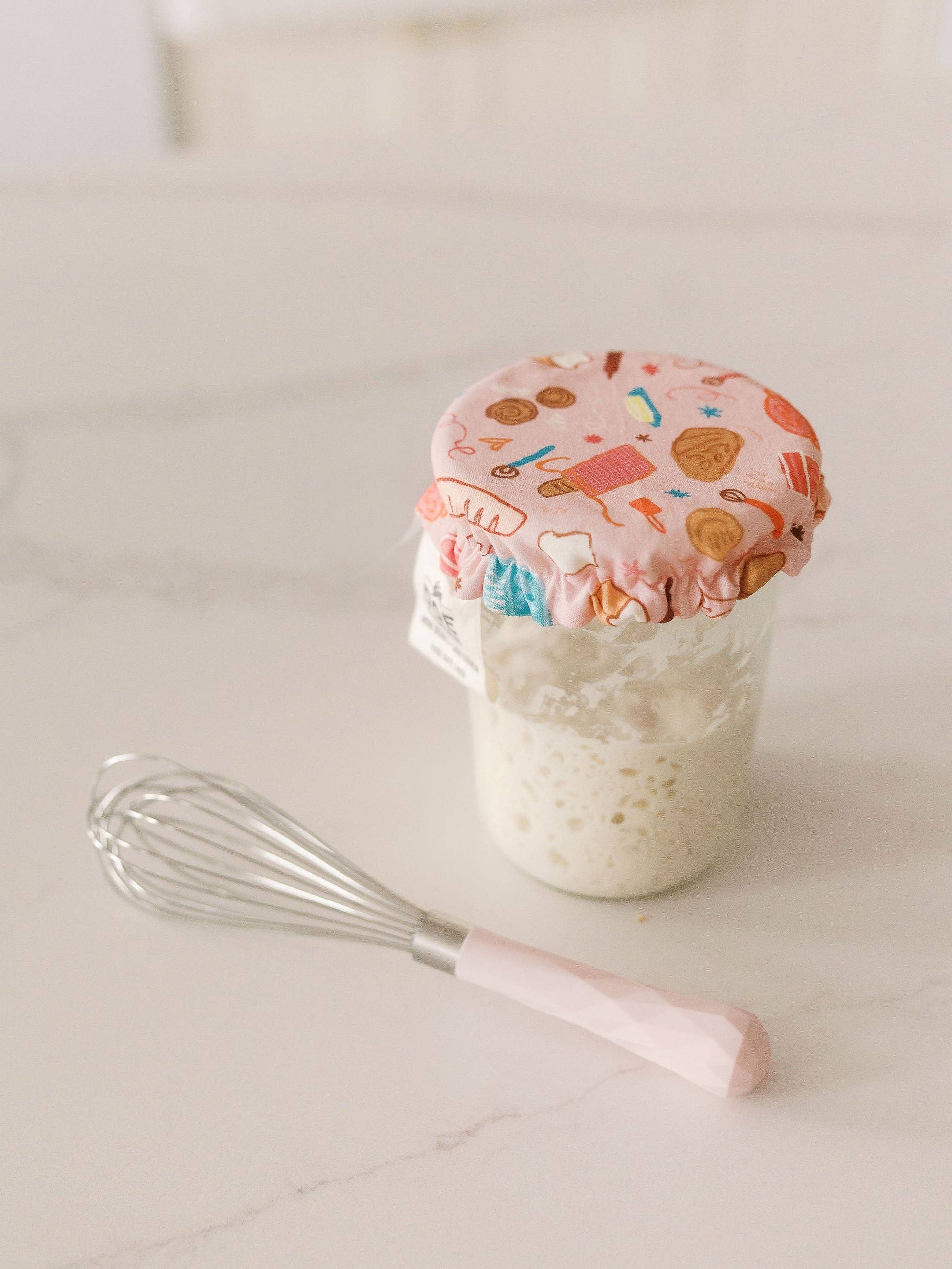 Jar of dough with a colorful lid and whisk on a light surface