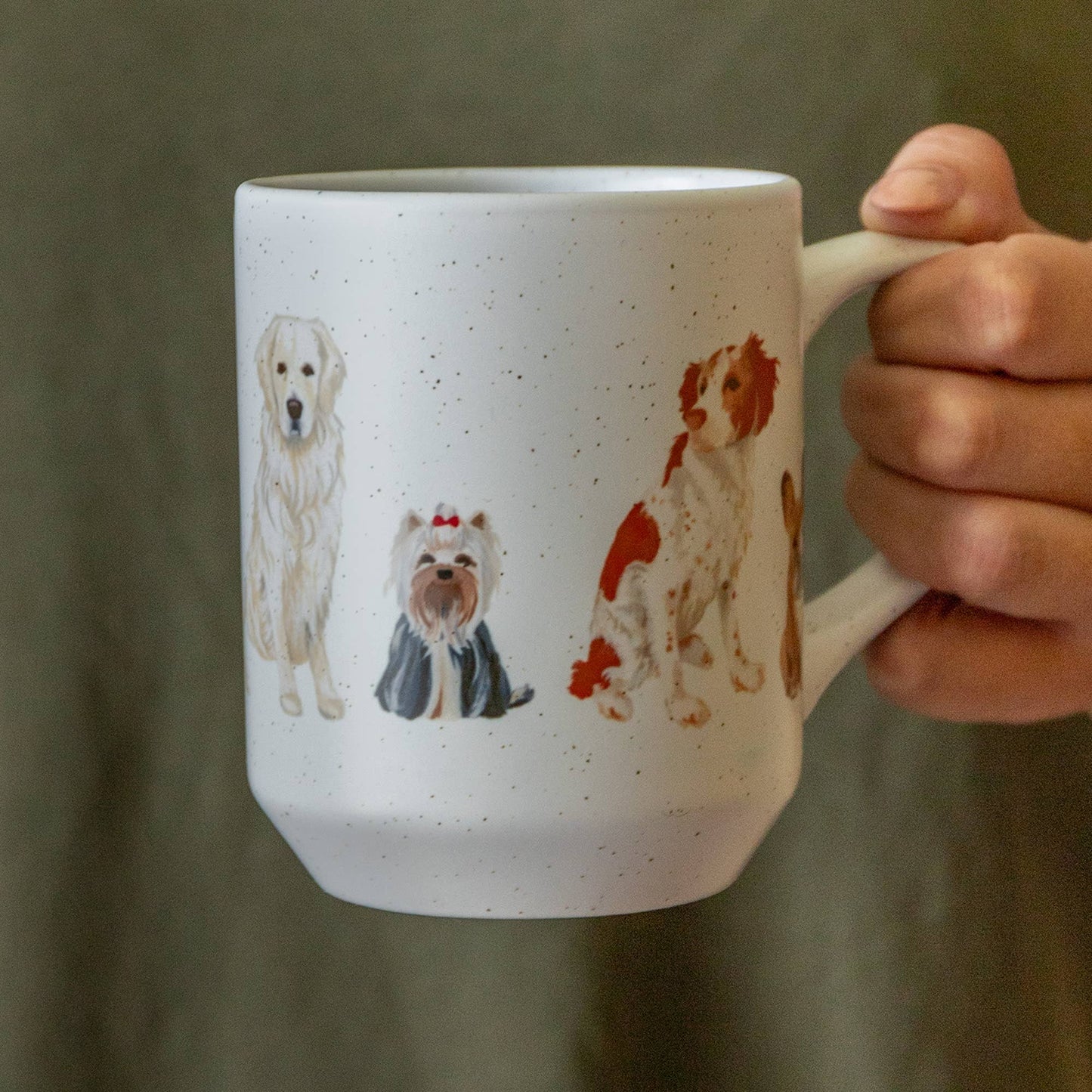 White mug with dog illustrations held by a hand against a green background