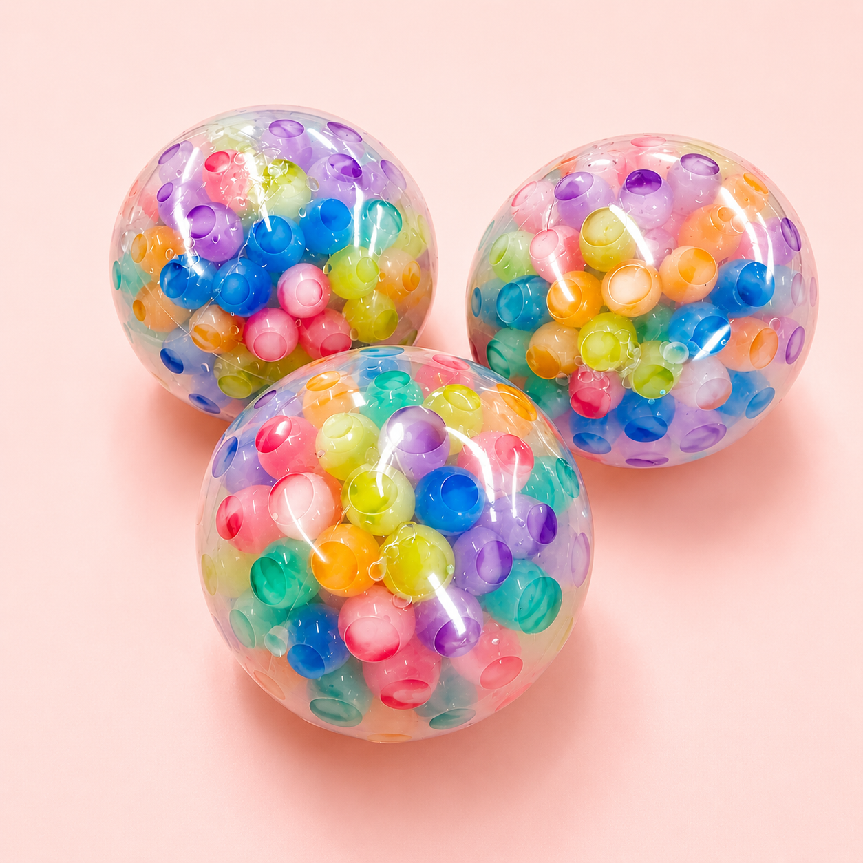 Three colorful transparent balls filled with multicolored beads on a pink background