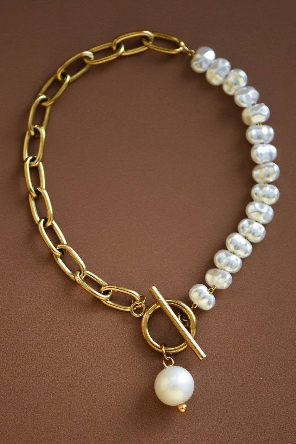 Bracelet with gold chain and pearl beads on a brown background