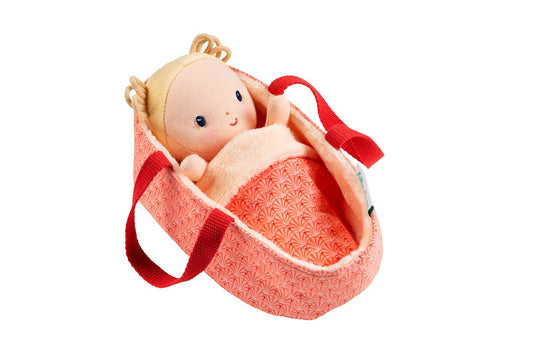 Baby doll in a pink bassinet with red straps on a white background
