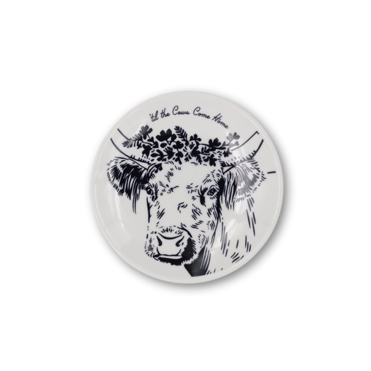 Round white plate with black cow illustration and floral design on a white background