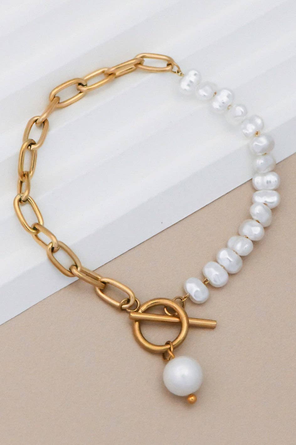 Gold chain bracelet with white pearls on a beige and white background