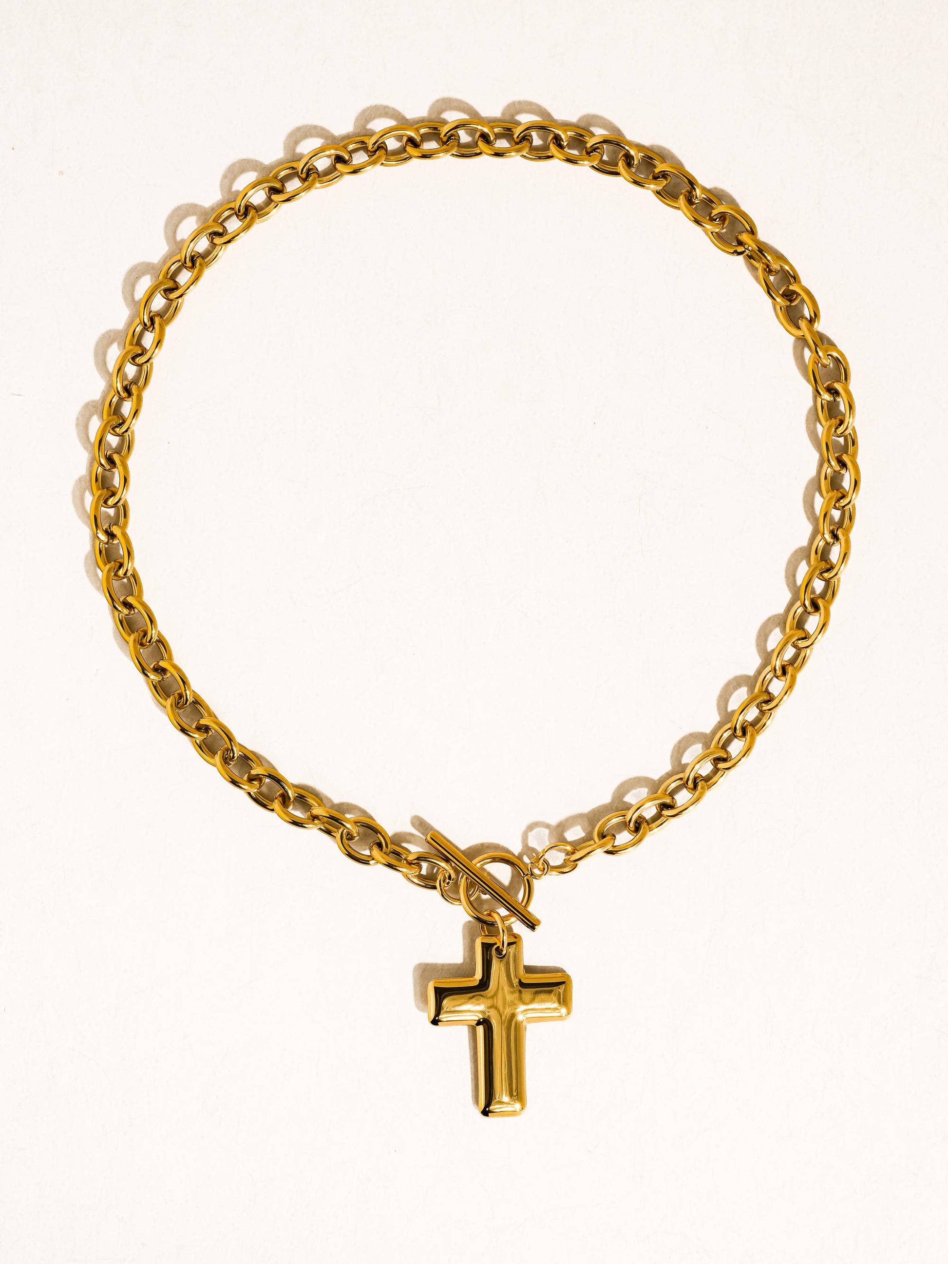 Gold chain bracelet with a cross pendant on a white background