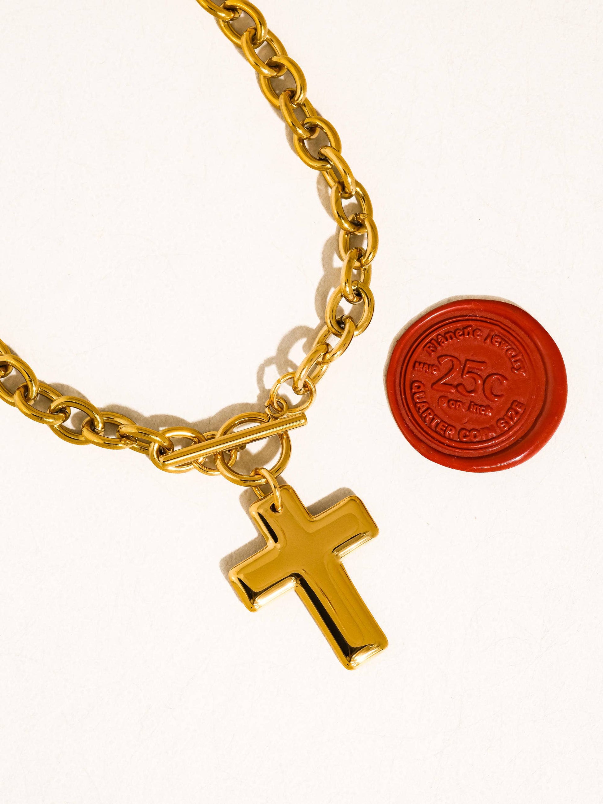 Gold chain bracelet with a cross charm and a red stamp on a white background