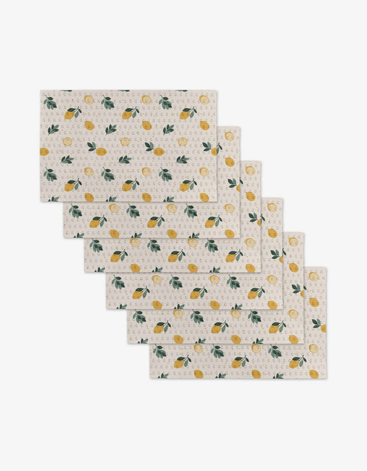 Six rectangular placemats with a lemon and citrus pattern on a cream background, arranged in a staggered stack on a light gray background.