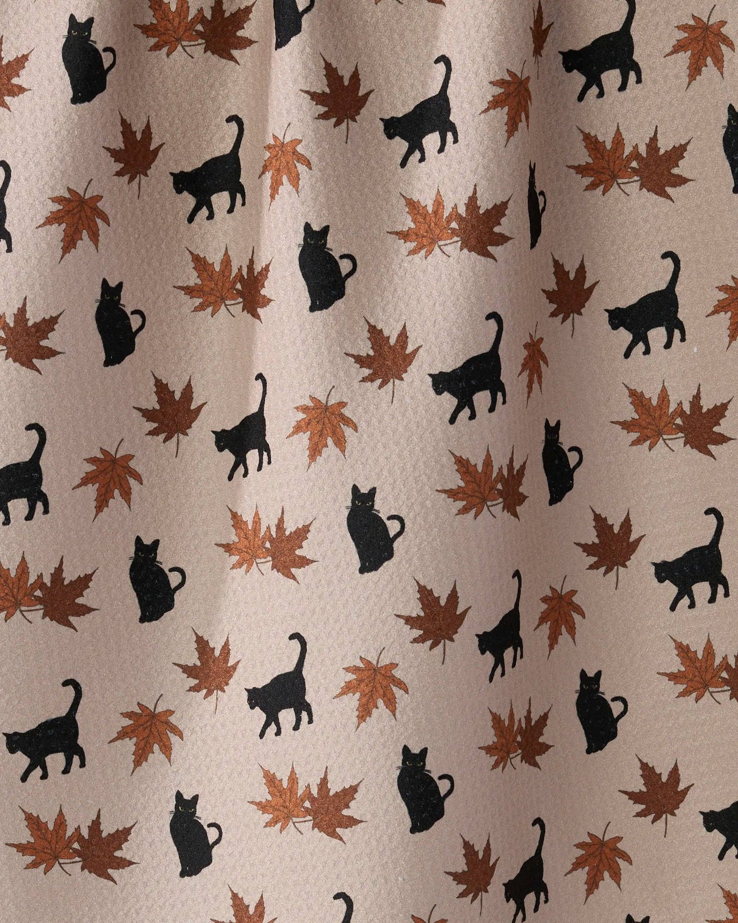 A close-up of a fabric or wallpaper pattern featuring black cat silhouettes and brown/orange autumn maple leaves on a light beige background.