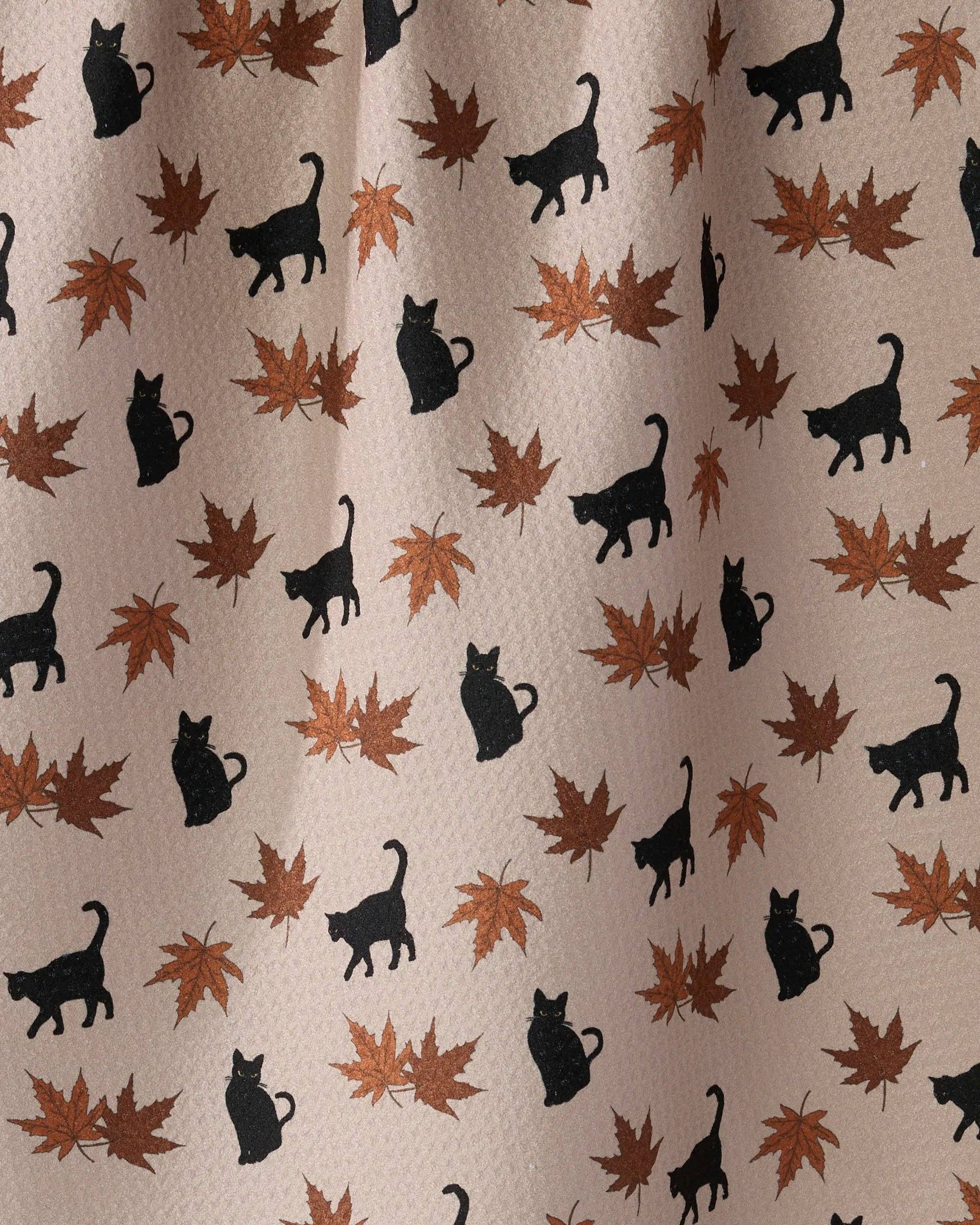 A close-up of a fabric or wallpaper pattern featuring black cat silhouettes and brown/orange autumn maple leaves on a light beige background.