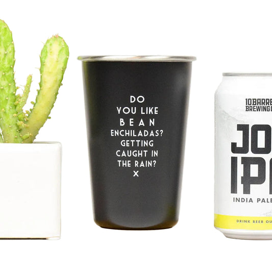 Black tumbler with text and a can of beer on a white surface with a cactus in the background