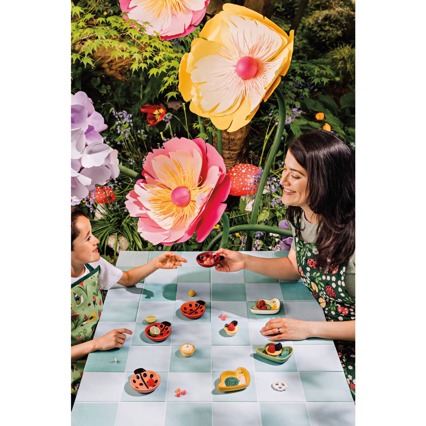 Two people sitting at a table with floral decorations and ladybug shaped bowls with snacks inside