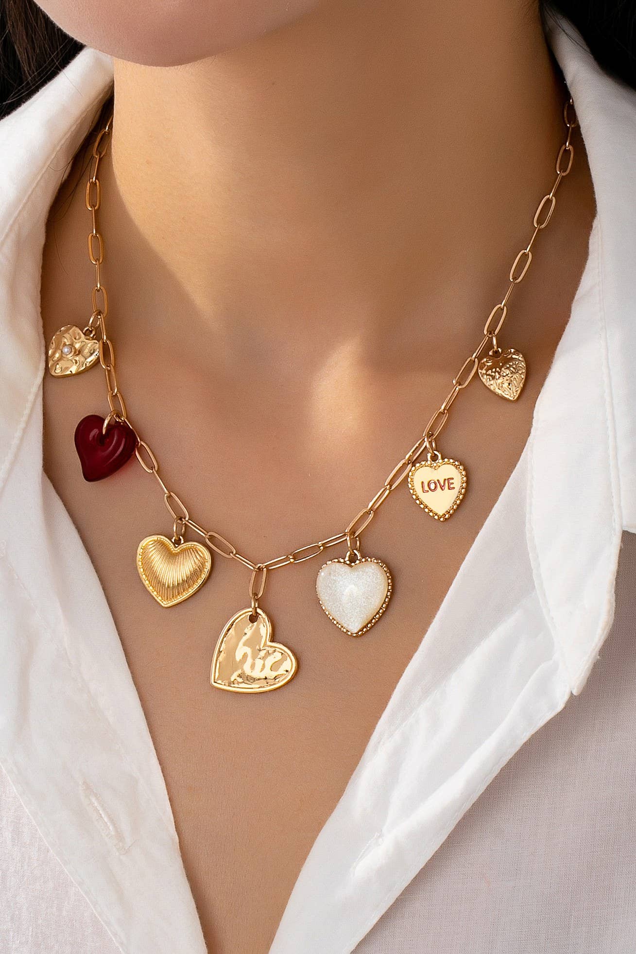 Woman wearing gold chain link necklace with different gold, pearl, and red heart charms