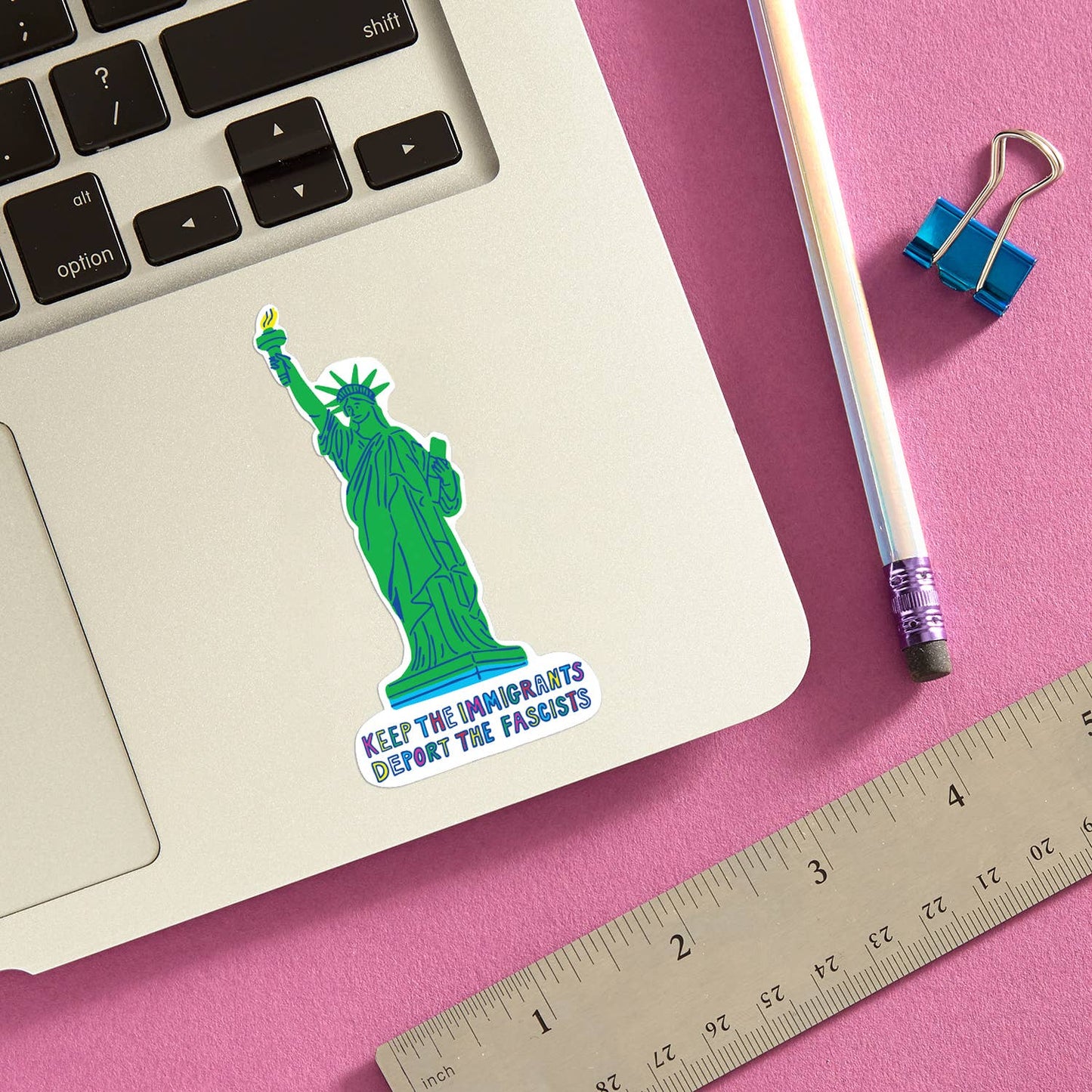 Laptop with a sticker of the Statue of Liberty on a pink surface with a pencil and ruler.
